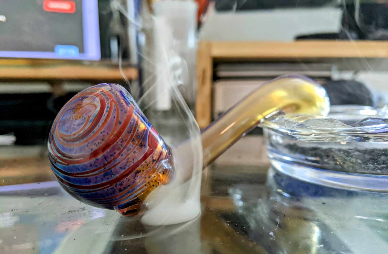 An image of a glass pipe used for smoking cannabis. Smoke is curling up from its bowl.